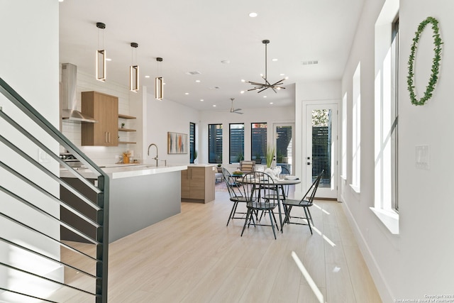 kitchen featuring decorative light fixtures, sink, light hardwood / wood-style flooring, a kitchen island with sink, and wall chimney exhaust hood