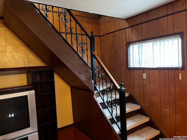 stairs featuring wood walls and a textured ceiling