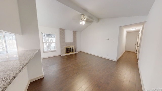 unfurnished living room with ceiling fan, dark wood-type flooring, brick wall, a brick fireplace, and lofted ceiling with beams