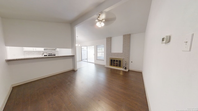 unfurnished living room with dark wood-type flooring, brick wall, ceiling fan, and a brick fireplace