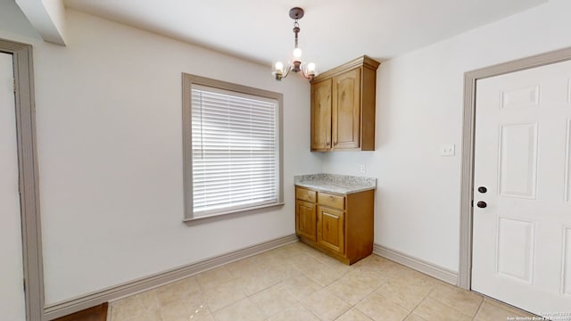 kitchen with light tile flooring, decorative light fixtures, a notable chandelier, and light stone counters