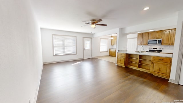 kitchen with stove, ceiling fan, tasteful backsplash, wood-type flooring, and sink