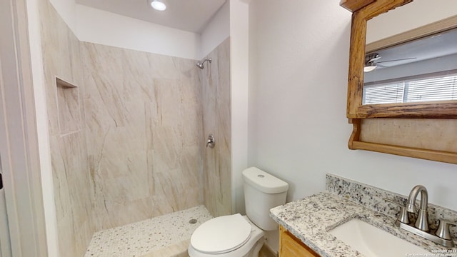 bathroom featuring ceiling fan, tiled shower, toilet, and oversized vanity