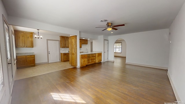 unfurnished living room with ceiling fan with notable chandelier, sink, and light hardwood / wood-style floors