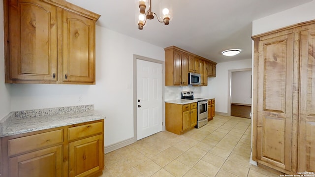 kitchen with an inviting chandelier, light stone counters, stainless steel appliances, light tile floors, and decorative light fixtures