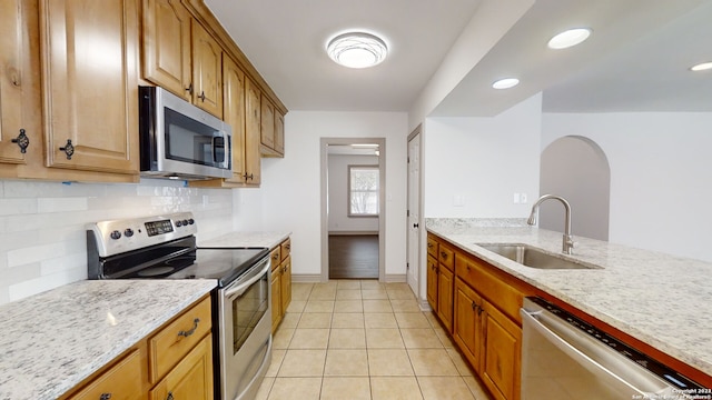 kitchen featuring appliances with stainless steel finishes, light stone countertops, sink, and light tile flooring