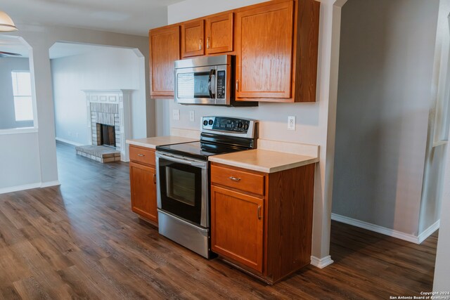 kitchen featuring a brick fireplace, stainless steel appliances, and dark wood-type flooring