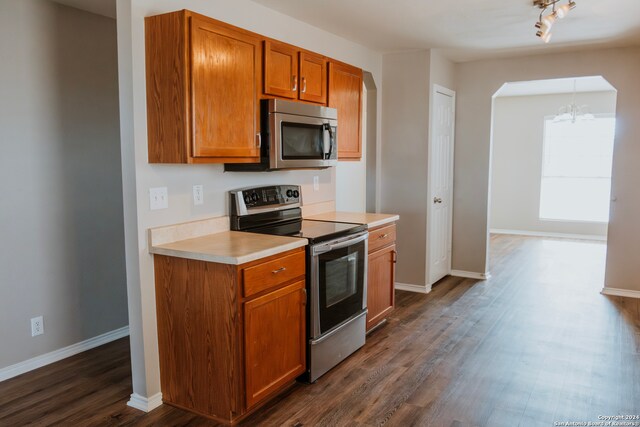 kitchen with track lighting, stainless steel appliances, dark wood-type flooring, and a notable chandelier