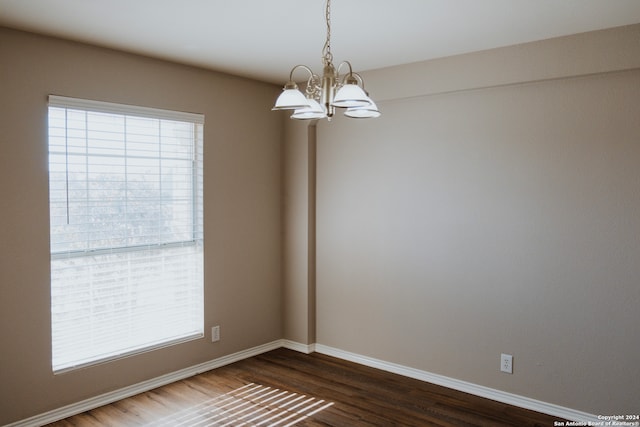 spare room with a wealth of natural light, dark wood-type flooring, and an inviting chandelier