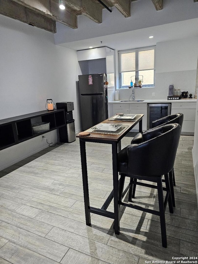 dining room featuring beam ceiling, wine cooler, light hardwood / wood-style flooring, and sink