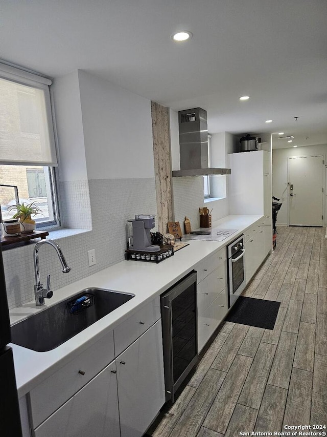 kitchen featuring wine cooler, tasteful backsplash, wall chimney exhaust hood, oven, and sink