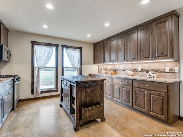 kitchen with dark brown cabinetry, appliances with stainless steel finishes, backsplash, light stone countertops, and a center island