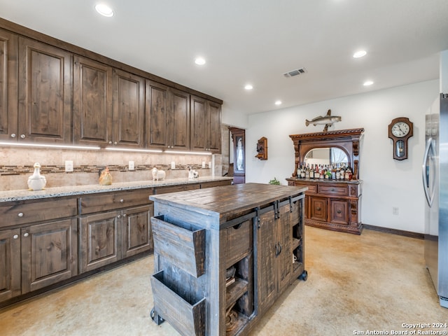 kitchen with backsplash, dark brown cabinetry, and stainless steel fridge