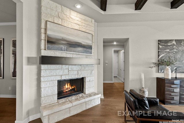 living room with dark wood-type flooring, beam ceiling, and a stone fireplace