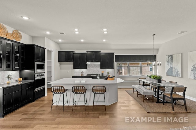 kitchen featuring decorative light fixtures, appliances with stainless steel finishes, light hardwood / wood-style floors, a center island with sink, and a chandelier