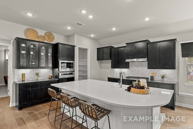 kitchen with a kitchen breakfast bar, a center island with sink, appliances with stainless steel finishes, and light wood-type flooring