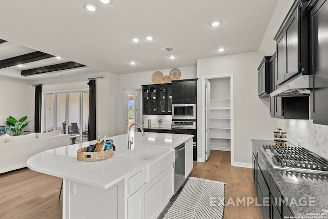 kitchen with an island with sink, beamed ceiling, light hardwood / wood-style flooring, and stainless steel appliances