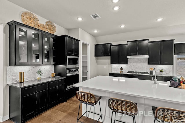 kitchen featuring stainless steel appliances, a kitchen breakfast bar, light hardwood / wood-style flooring, backsplash, and light stone counters