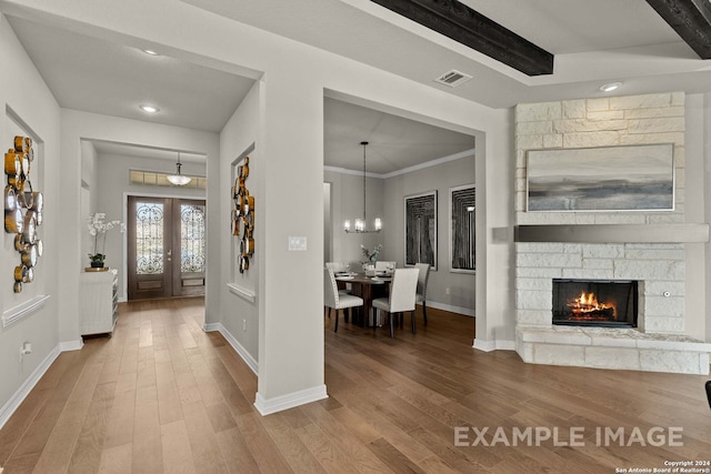 entrance foyer with a notable chandelier, dark hardwood / wood-style flooring, a stone fireplace, crown molding, and french doors