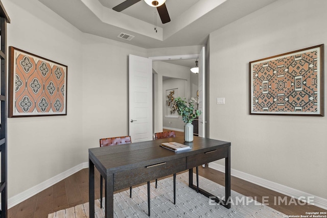 home office with ceiling fan, a raised ceiling, and dark hardwood / wood-style flooring