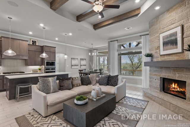 living room with a stone fireplace, light hardwood / wood-style flooring, ceiling fan with notable chandelier, ornamental molding, and a tray ceiling