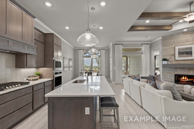 kitchen with ceiling fan, a stone fireplace, appliances with stainless steel finishes, a kitchen island with sink, and sink