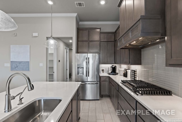 kitchen with dark brown cabinets, stainless steel appliances, pendant lighting, premium range hood, and sink