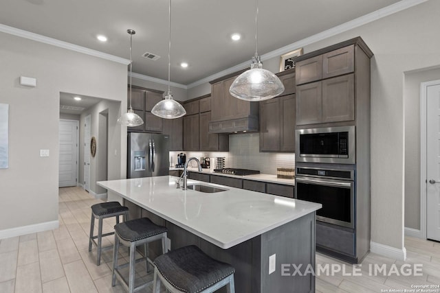 kitchen with backsplash, appliances with stainless steel finishes, sink, a center island with sink, and pendant lighting