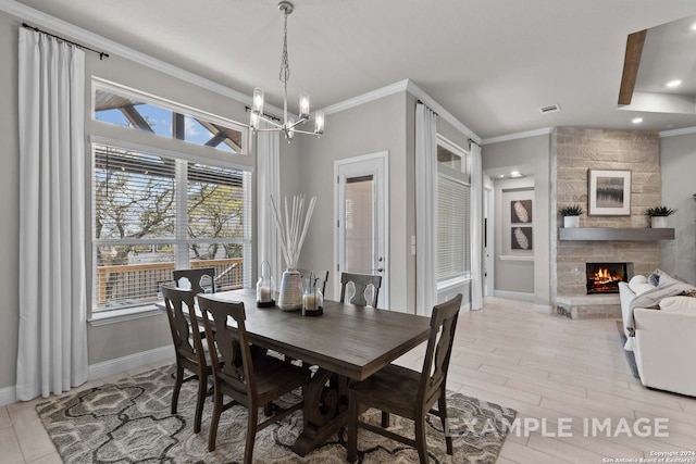 dining area with plenty of natural light, ornamental molding, a stone fireplace, and a notable chandelier