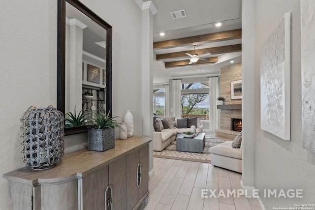 living room with ceiling fan, beamed ceiling, a fireplace, light wood-type flooring, and ornamental molding