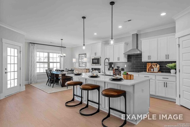 kitchen with a kitchen island with sink, white cabinetry, light hardwood / wood-style flooring, and wall chimney range hood