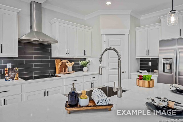 kitchen with stainless steel refrigerator with ice dispenser, wall chimney exhaust hood, white cabinets, and hanging light fixtures