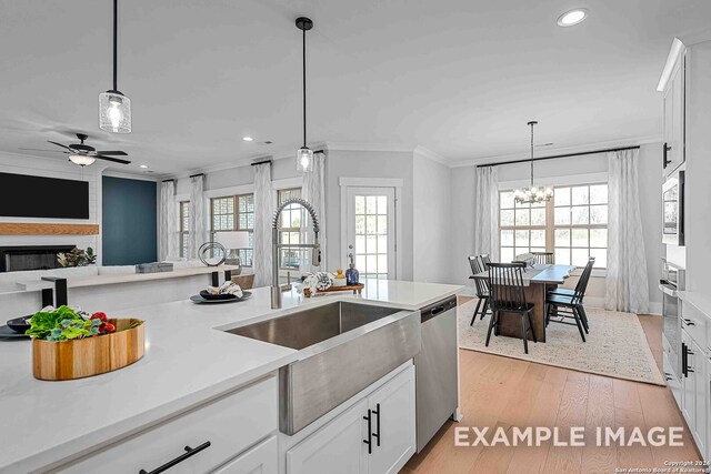 kitchen featuring ceiling fan with notable chandelier, a fireplace, light hardwood / wood-style flooring, stainless steel appliances, and white cabinets