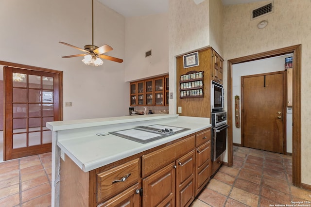 kitchen with kitchen peninsula, ceiling fan, a high ceiling, and appliances with stainless steel finishes