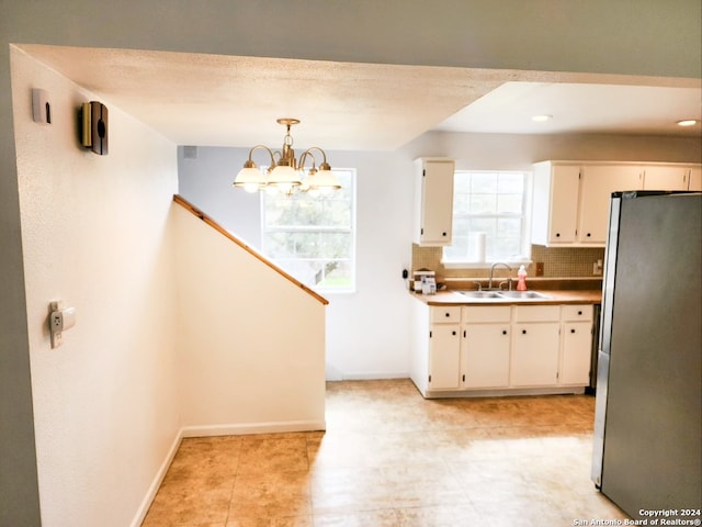 kitchen with pendant lighting, a notable chandelier, tasteful backsplash, stainless steel fridge, and sink