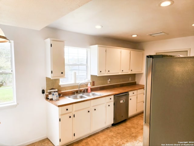 kitchen featuring stainless steel appliances, light tile floors, tasteful backsplash, white cabinetry, and sink