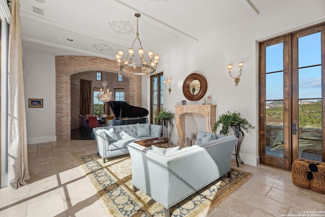 tiled living room with brick wall, french doors, a wealth of natural light, and an inviting chandelier