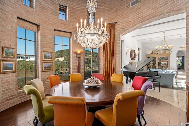 dining space featuring a towering ceiling, a notable chandelier, and brick wall