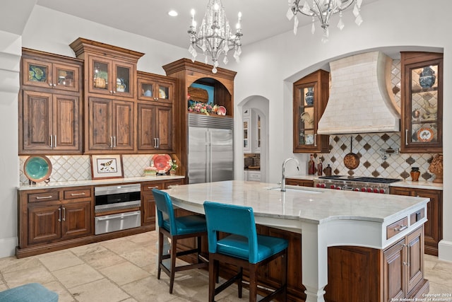 kitchen with decorative backsplash, a kitchen island with sink, premium range hood, and stainless steel appliances