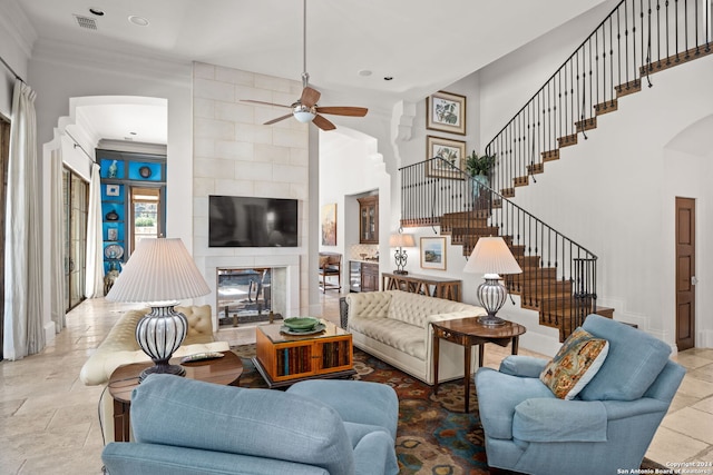 living room with ceiling fan, tile walls, tile patterned flooring, a tile fireplace, and ornamental molding