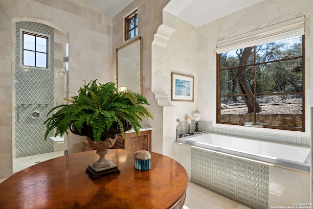 bathroom with a wealth of natural light, tiled bath, and tile patterned flooring