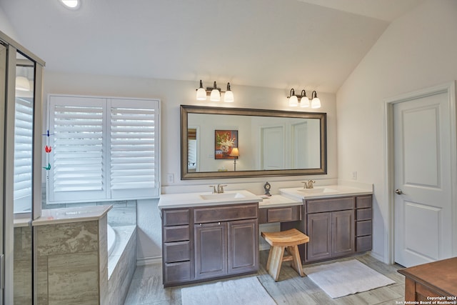 bathroom with lofted ceiling, hardwood / wood-style floors, tiled bath, and vanity