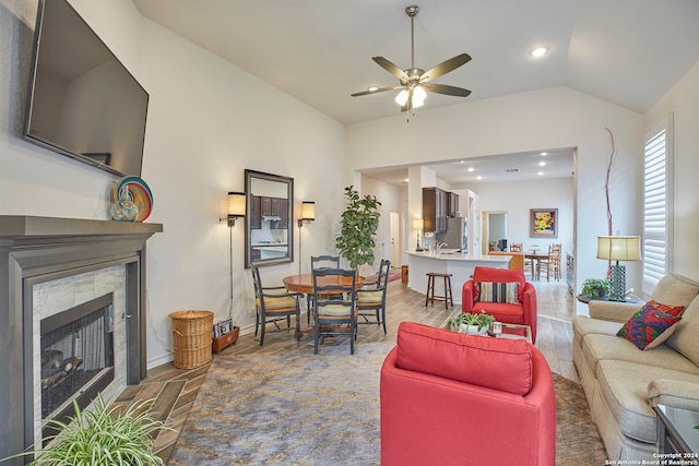 living room with ceiling fan, lofted ceiling, a tiled fireplace, and wood-type flooring