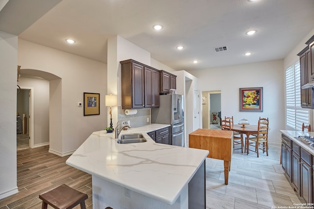 kitchen with light stone counters, sink, kitchen peninsula, stainless steel refrigerator with ice dispenser, and light wood-type flooring