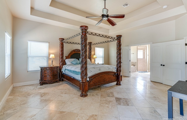 bedroom featuring ensuite bathroom, a raised ceiling, and multiple windows