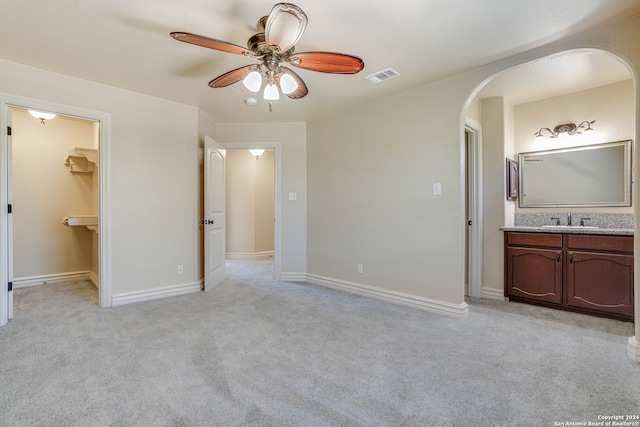 unfurnished bedroom with connected bathroom, a spacious closet, sink, ceiling fan, and light colored carpet