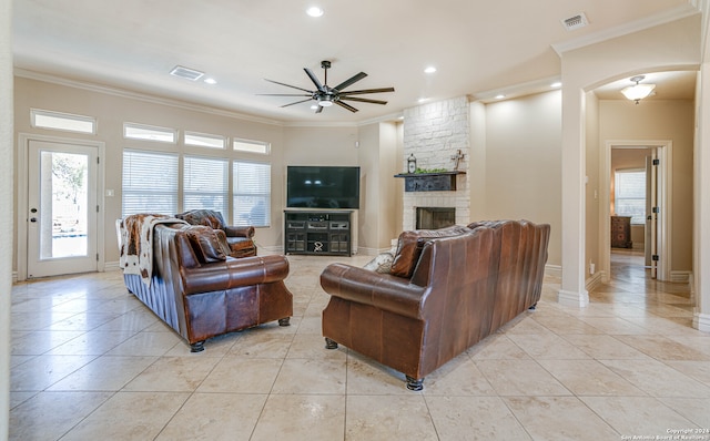 living room featuring a stone fireplace, ceiling fan, and crown molding