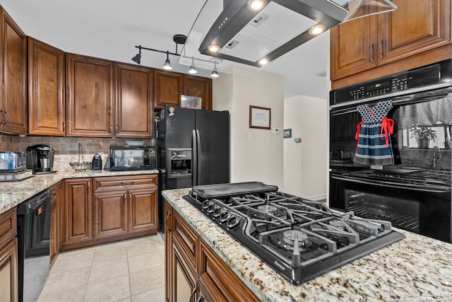 kitchen with island range hood, light tile floors, light stone countertops, tasteful backsplash, and black appliances