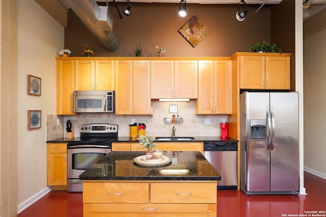 kitchen featuring backsplash, sink, stainless steel appliances, dark stone countertops, and a kitchen island