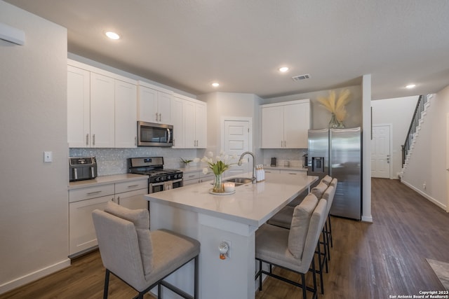 kitchen with dark hardwood / wood-style floors, a kitchen island with sink, appliances with stainless steel finishes, a breakfast bar area, and white cabinetry